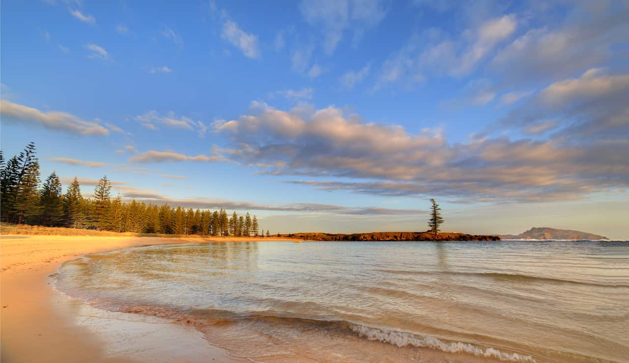 A photo taken from close to ground-level shows small ripples breaking onto a sandy beach under a blue sky. 