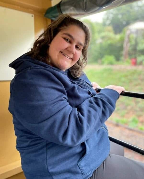 A woman in a blue hoodie sitting with her legs out the side of the Puffing Billy train