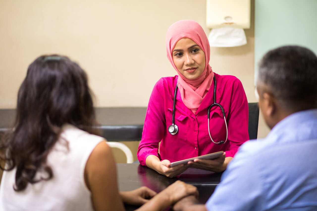 A female doctor wearing a headscarf speaks with a man and a woman.