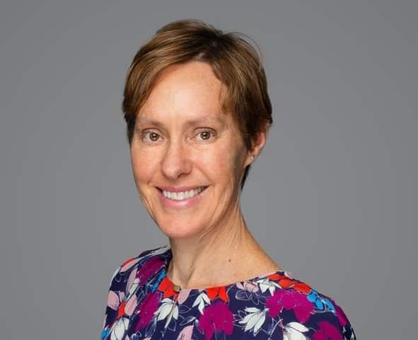 A woman with short hair, wearing a coloureful patterned blouse