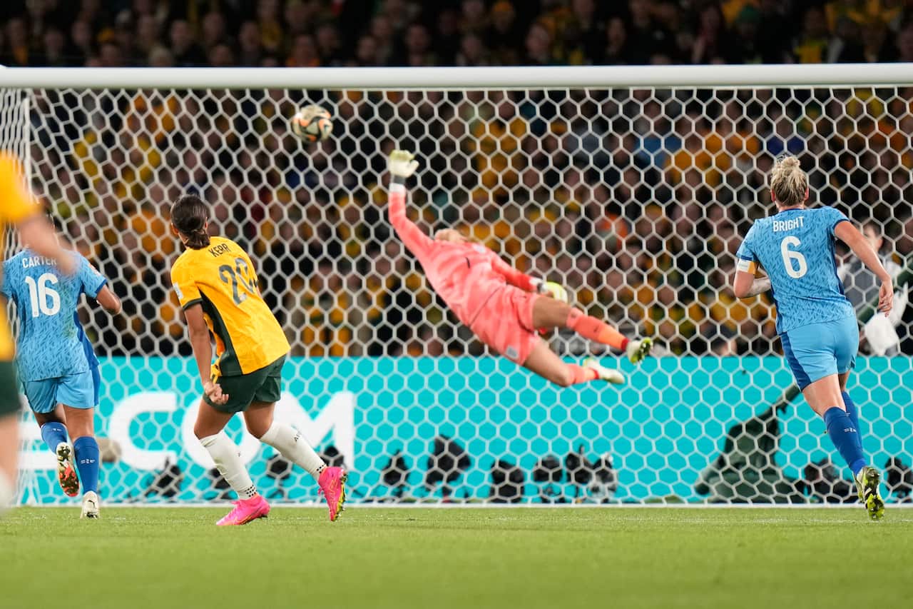 A woman with a yellow football jersey scores a goal, as a goalie with a pink football jersey jumps for the ball. 