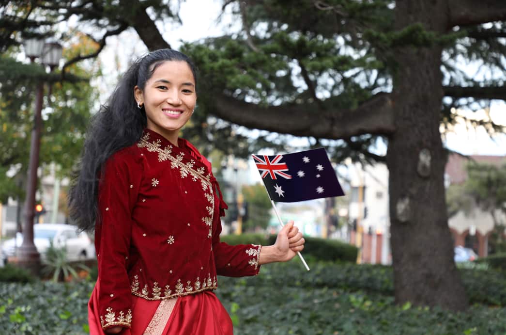 A young Nepali woman smiling and holding an Australian flag. She is wearing a red dress. 