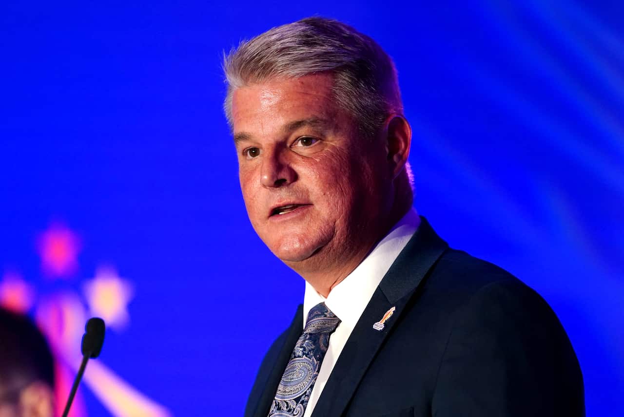 A man wearing a suit and tie speaking in front of a microphone.