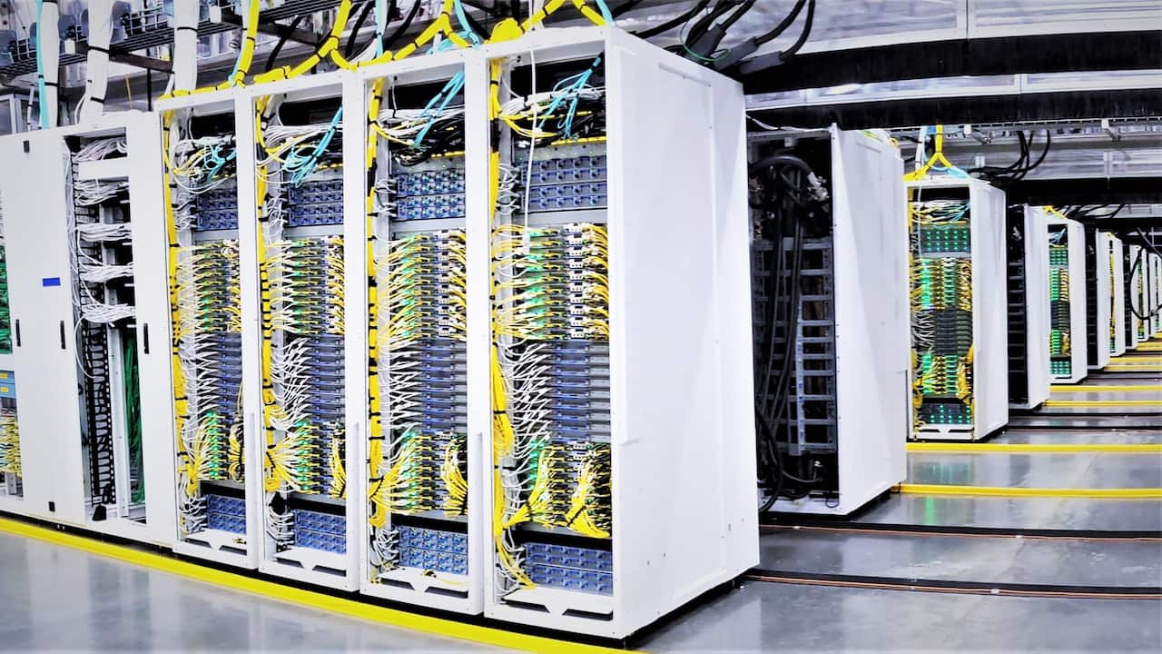 Rows of AI data processing computers stand inside a large warehouse.