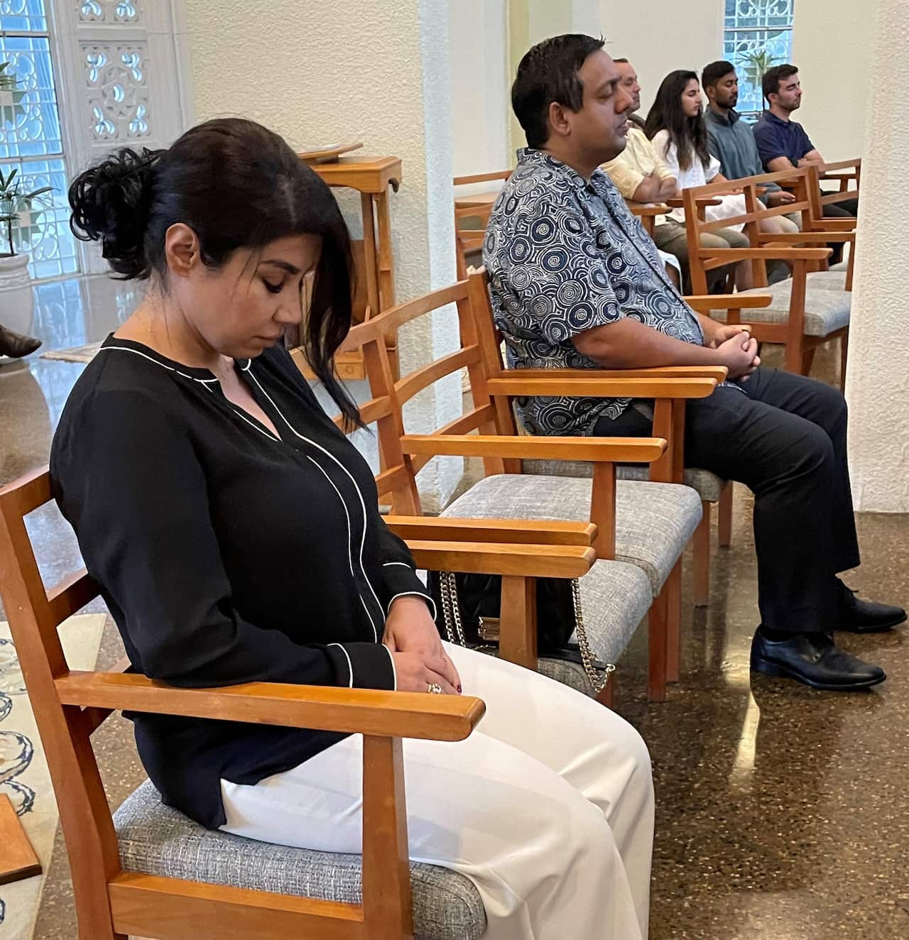 A woman in a black shirt sitting on a chair with her head tilted forward. 