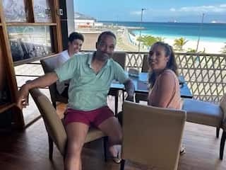 A man with his wife and son sitting on a seat in a balcony, smiling. A beach is in the background.
