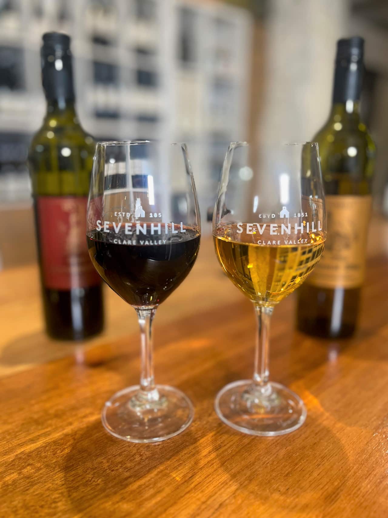 Half filled glasses of red and white wine sit next to botles on a table.