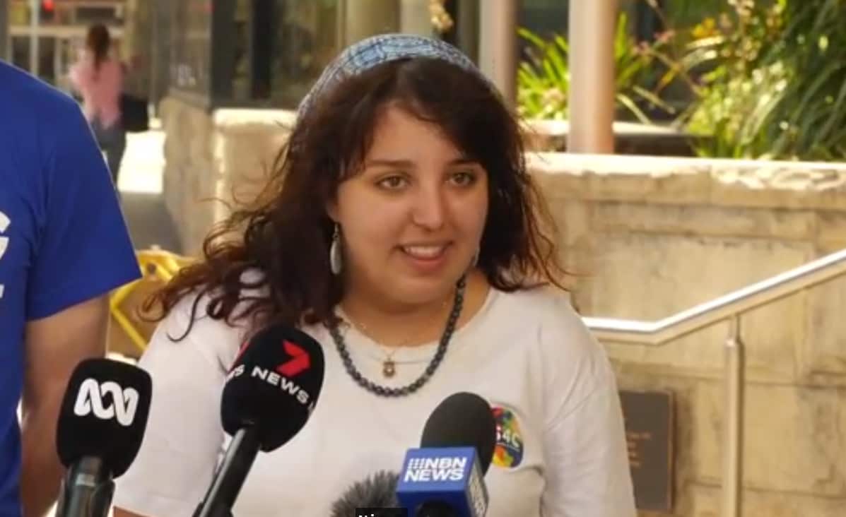 A teenager in a white shirt standing in front of microphones