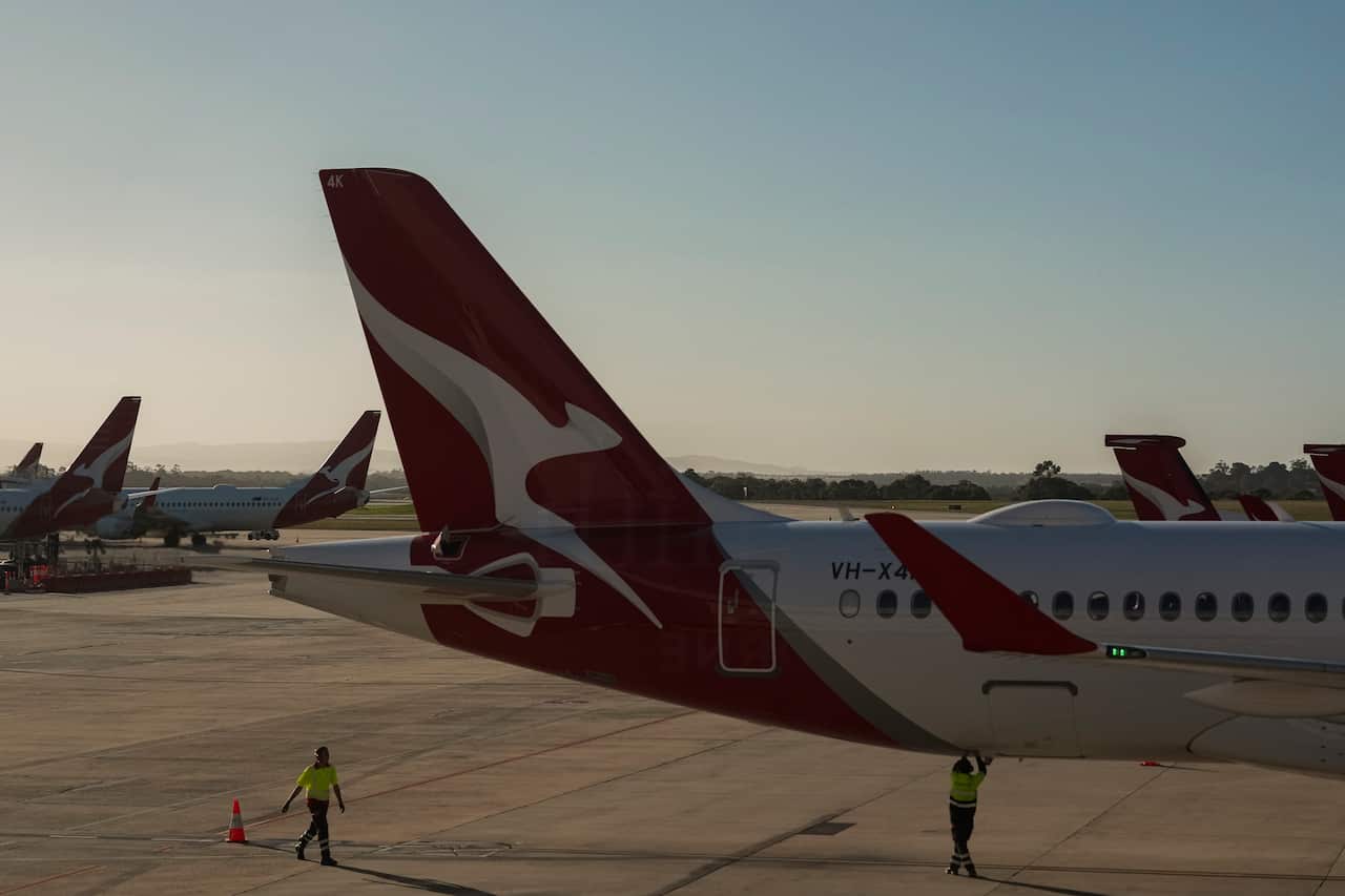 The tail of a Qantas plane is visible as it sits on the tarmac.