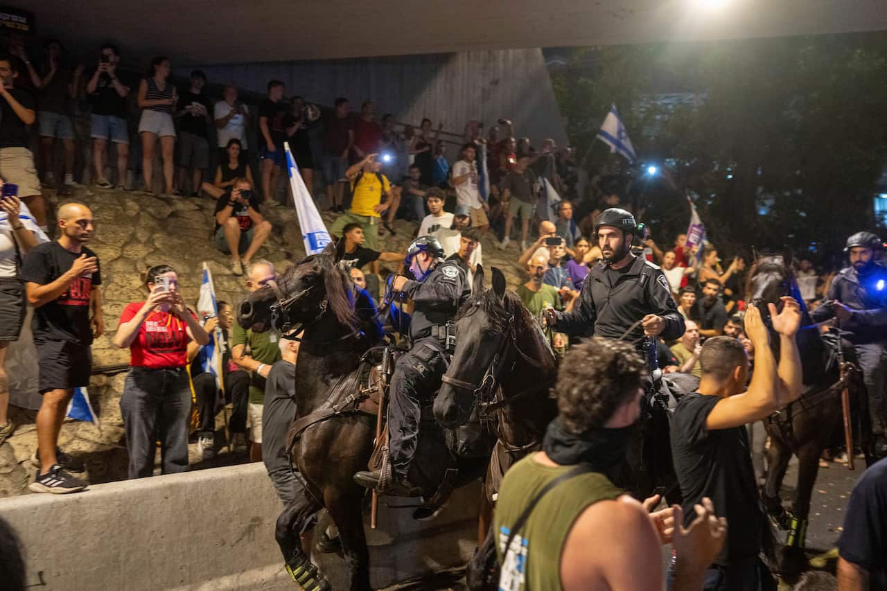 A group of protesters standing in the streets and on a hill as Israeli police ride horses.