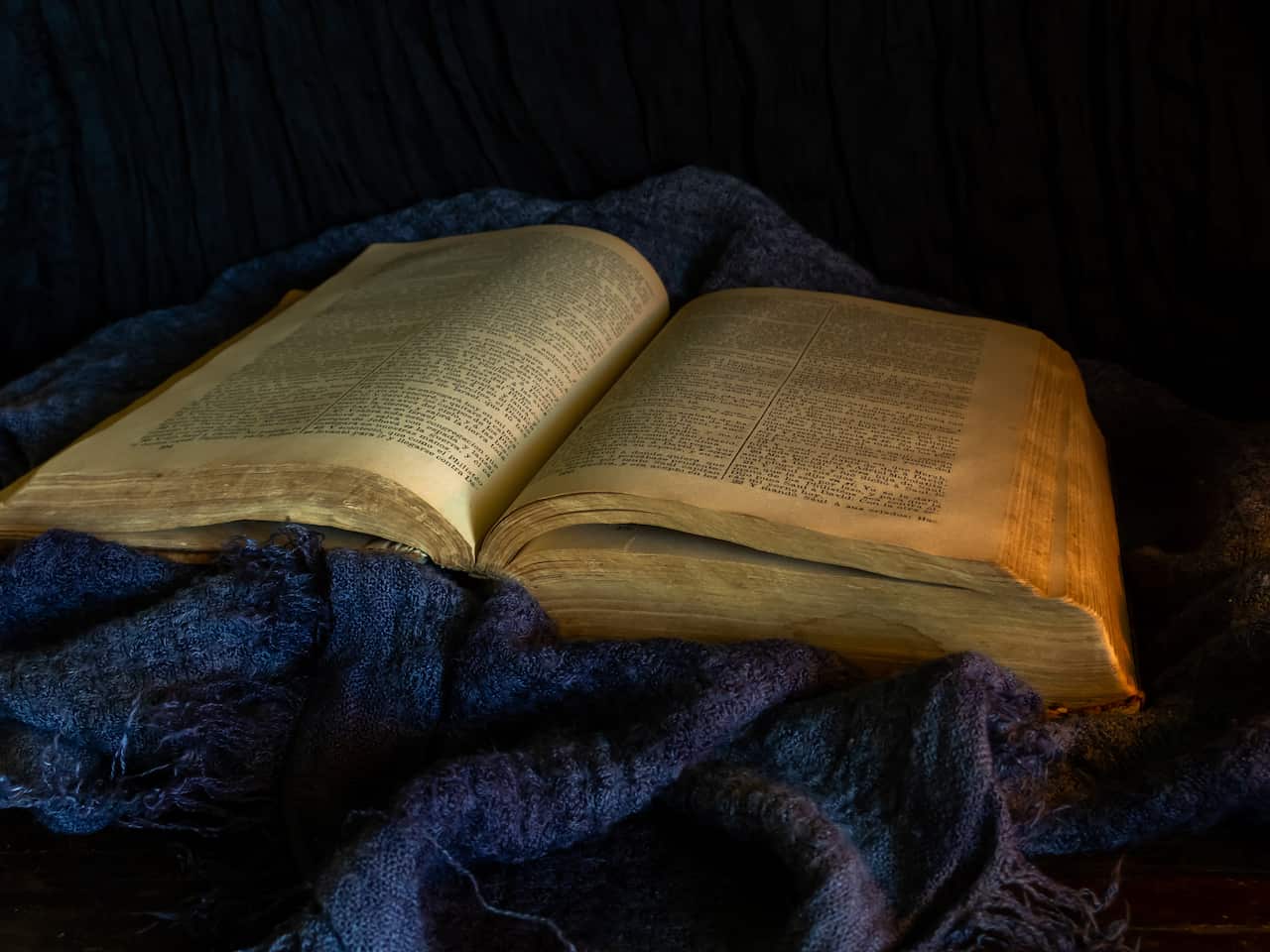 A still life with an open ancient bible on a dark old cloth.