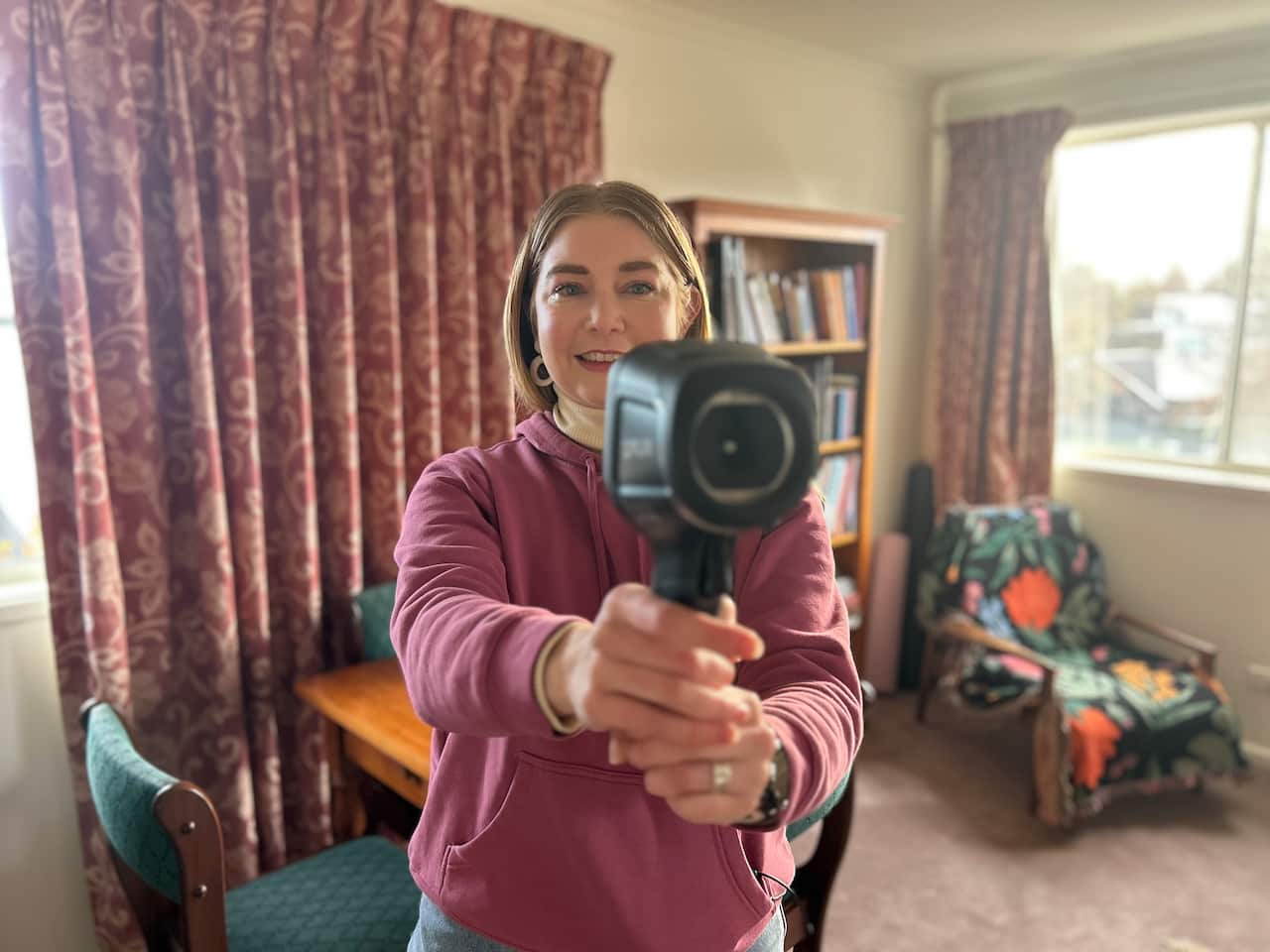 A woman holds a thermal camera up, pointing it at the person taking a photograph of her.