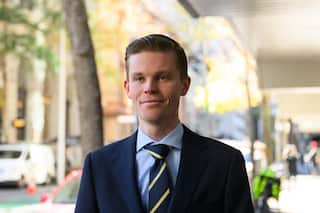 Dylan Whitelaw in a blue suit and a yellow striped tie with short hair walking down a city street on a bright day
