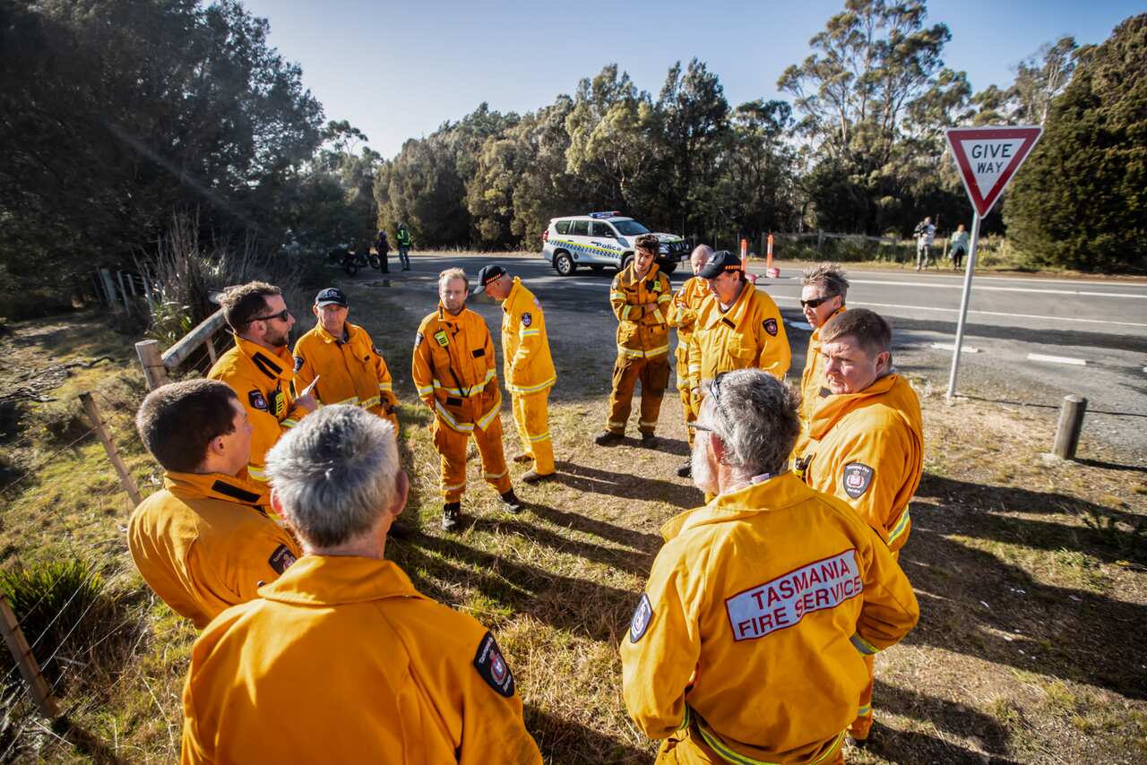 Around 10 Tasmania Fire Service crew stand in a circle next to a road.