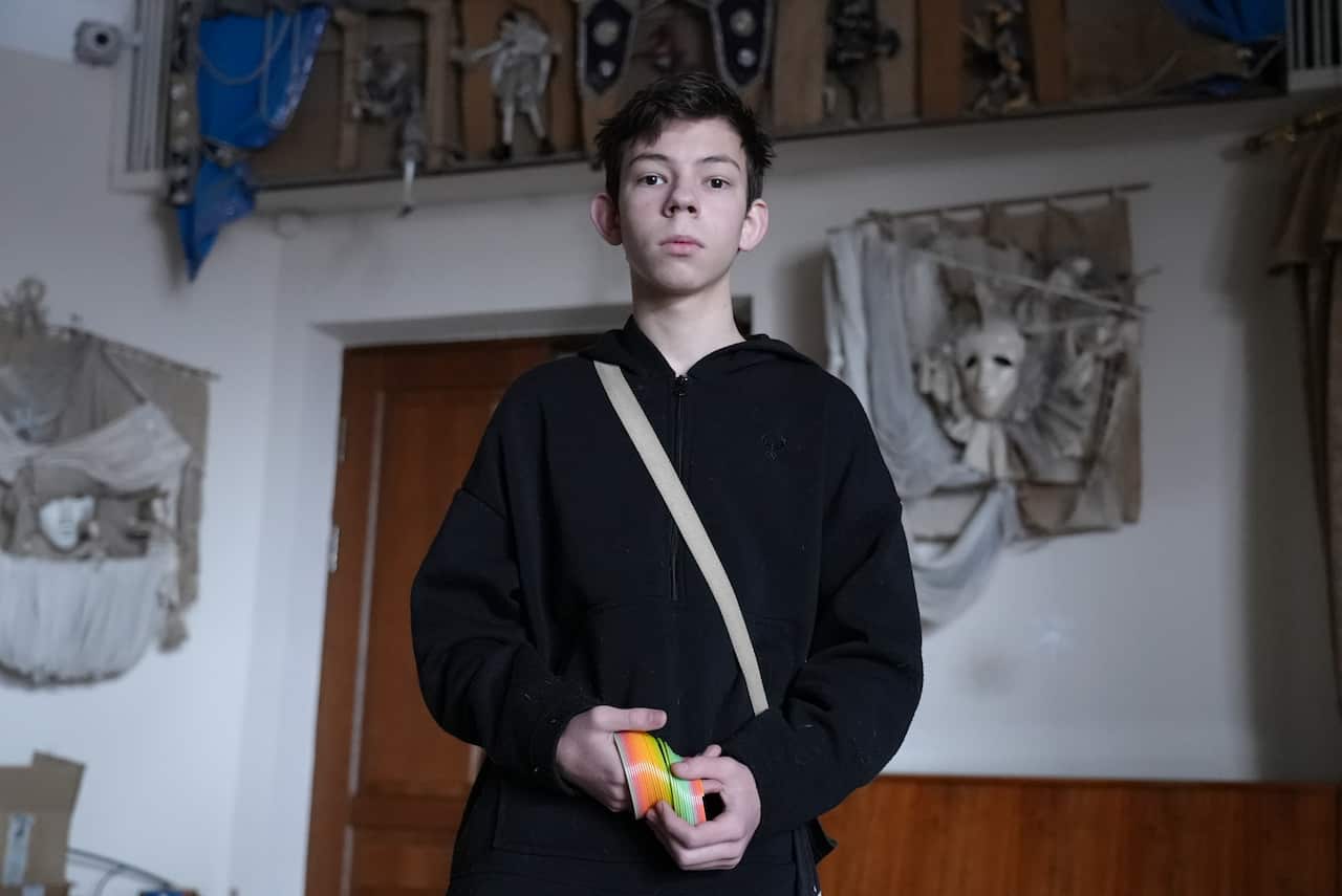 A 16-year-old boy holds a rainbow-coloured slinky in his hands while standing inside.