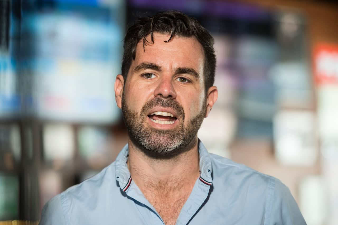 A man in a blue shirt speaking in front of a blurred background