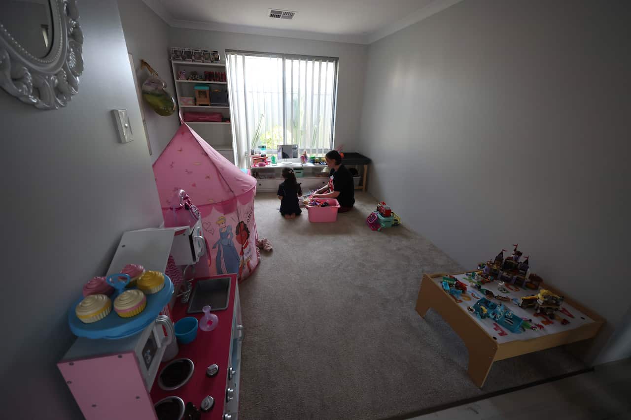 Wide shot of mother and daughter playing inside a home, with pink and girl toys everywhere.