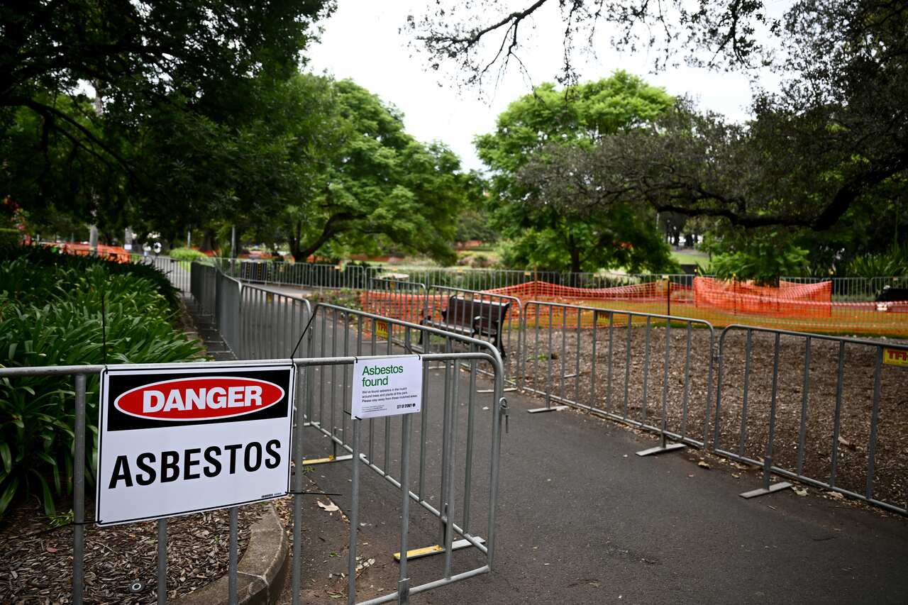 A temporary fence blocks the park entrance with a sign warning of asbestos danger.