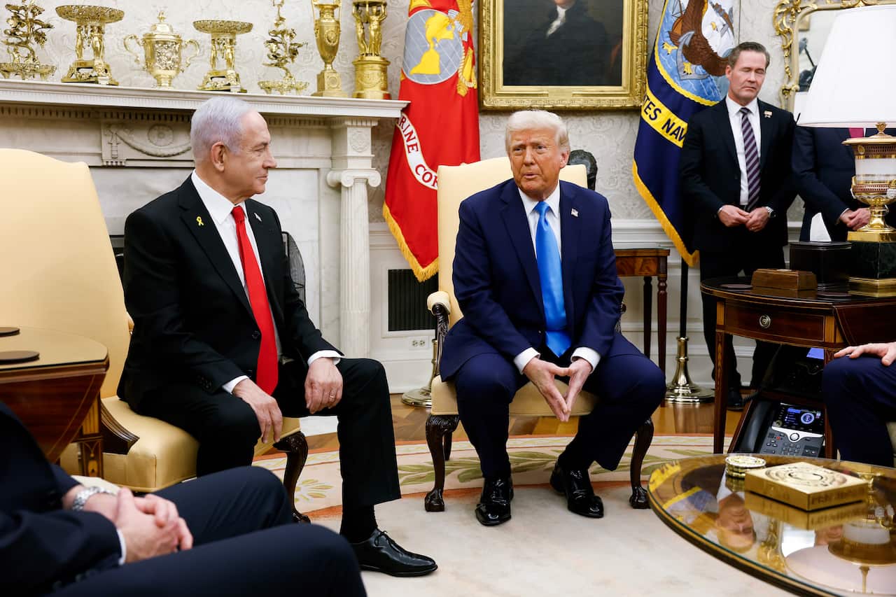 Two men in suits sit next to each other in chairs at the White House.