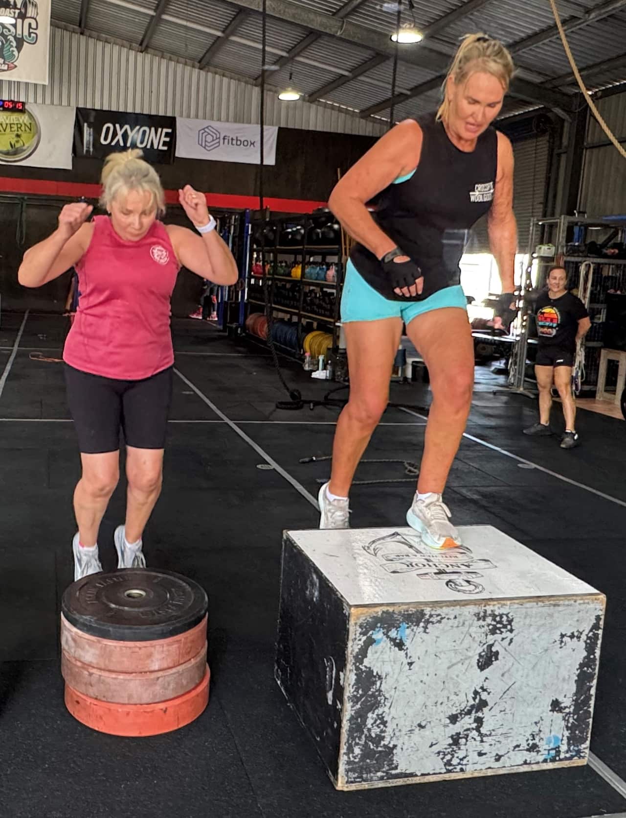 Two women in active wear work out together at a gym.