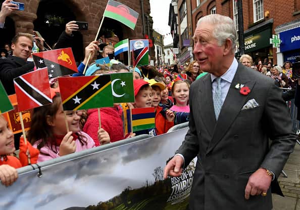 Prince Charles (right) talks to children holding flags of different countries and standing behind a street barrier at a festival in England.