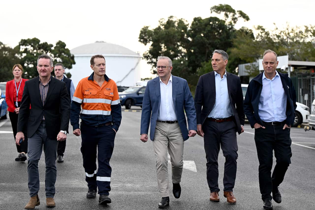 Chris Bowen, a man in an orange hi-vis jumpsuit, Anthony Albanese, Richard Marles and a man in a black suit and white shirt walking down a pathway.