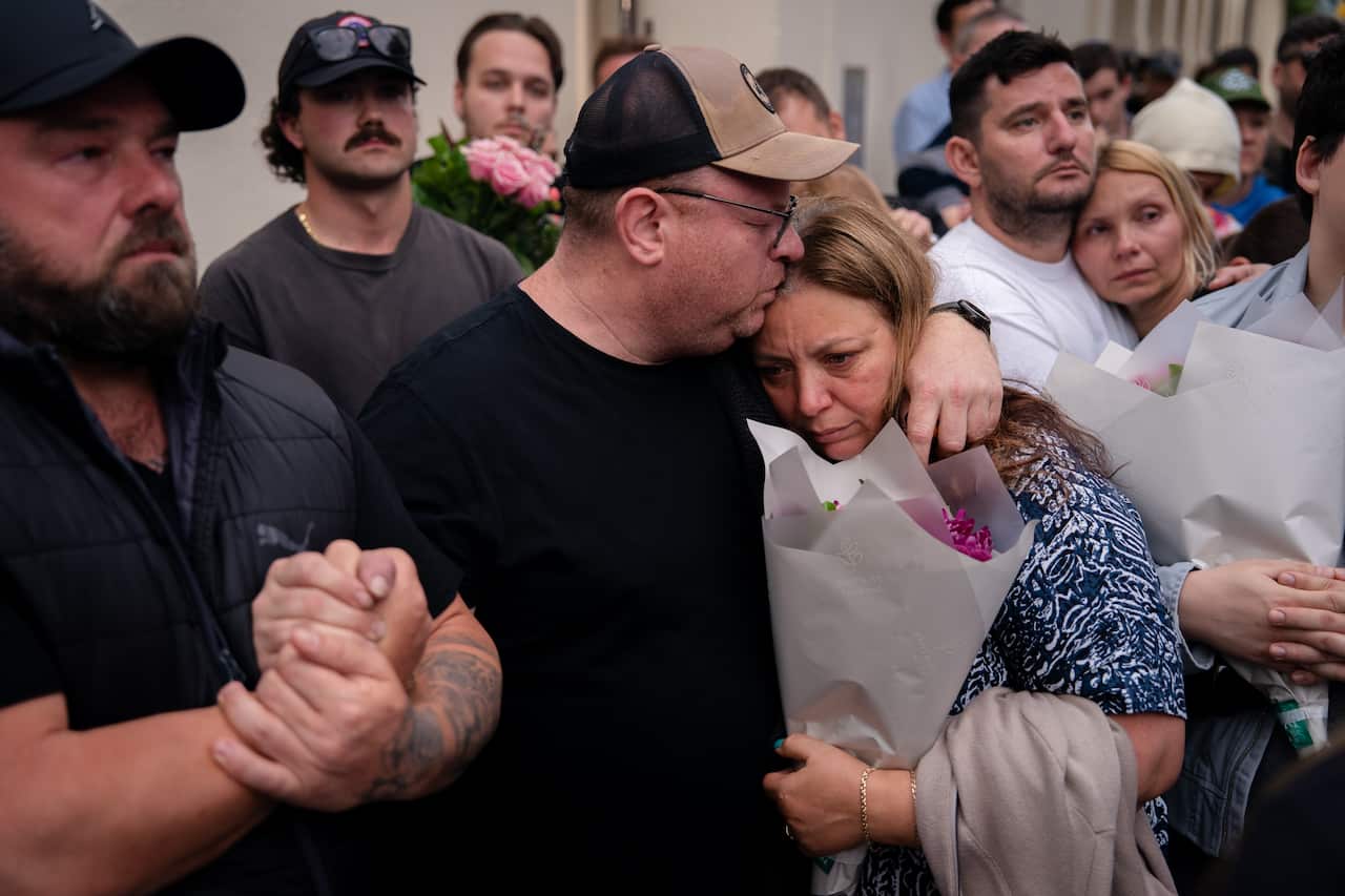 People holding flowers and embracing at a memorial for victims of a mass shooting