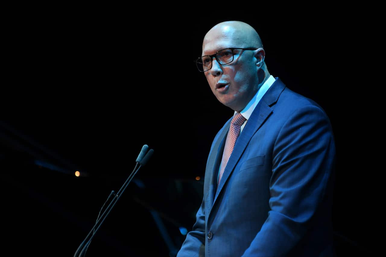 A man wearing a suit, tie, and glasses standing at a lectern and speaking into a microphone.