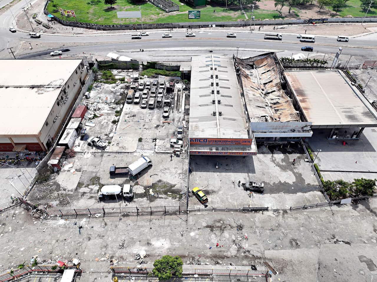 A shopping center in Port Moresby is in ruins with a damaged roof and remnants of cars in the parking lot.