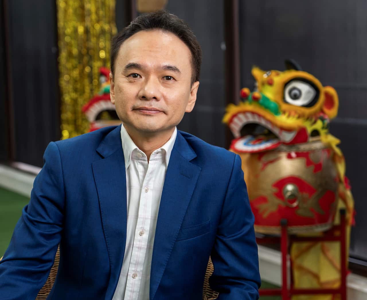 A man in a bue suit jacket sits near a colourful Chinese dragon.