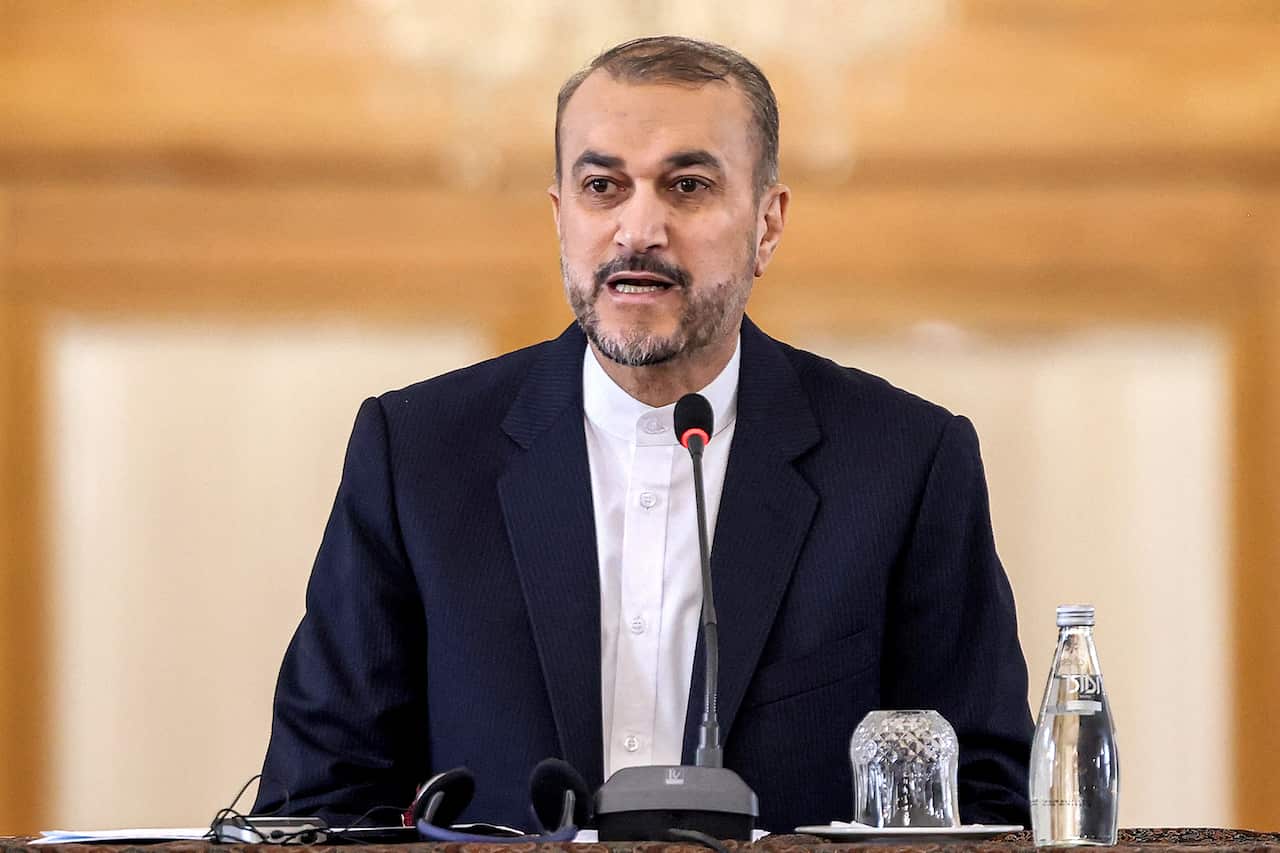 A man wearing a dark suit jacket and white shirt speaking into a microphone 