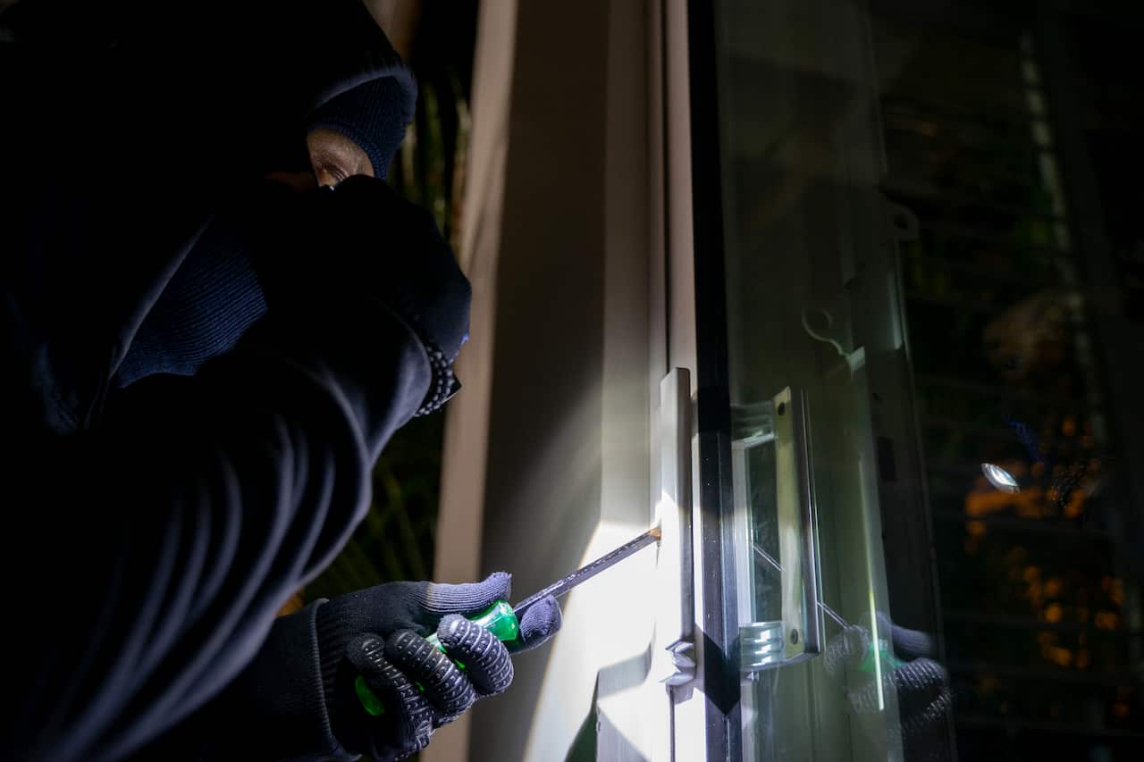 A dangerous masked thief with a crowbar breaks into the door of the victim's house.