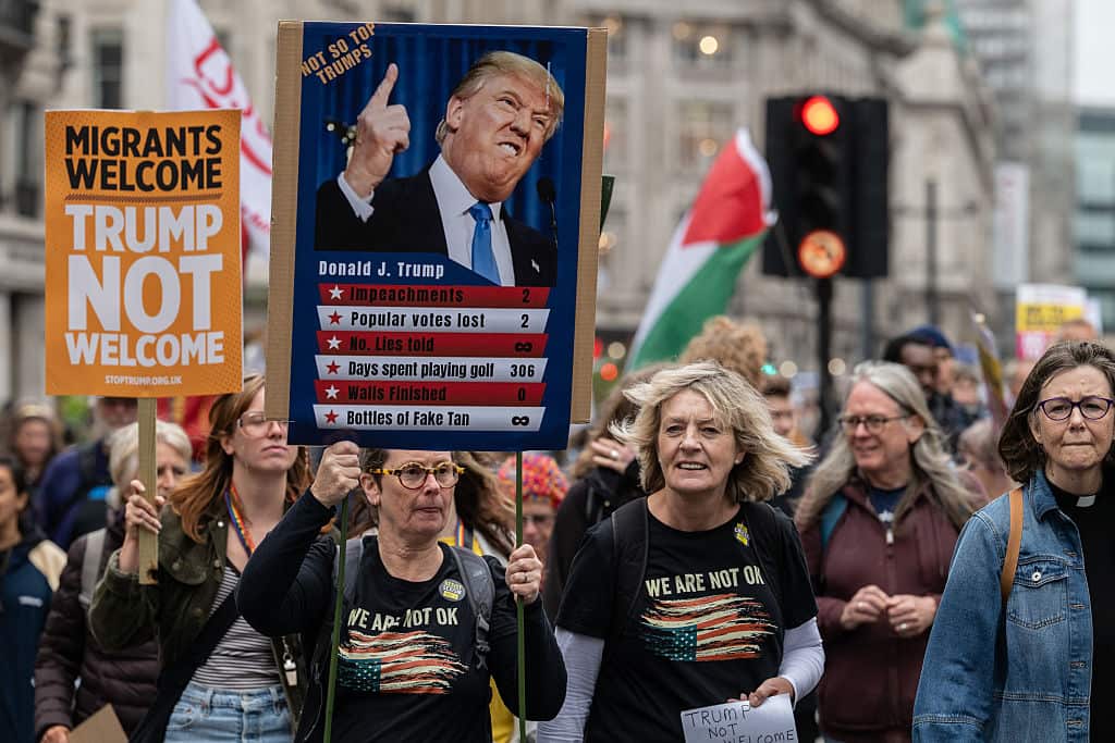 Protesters holding placards denouncing Donald Trump's visit during a march.