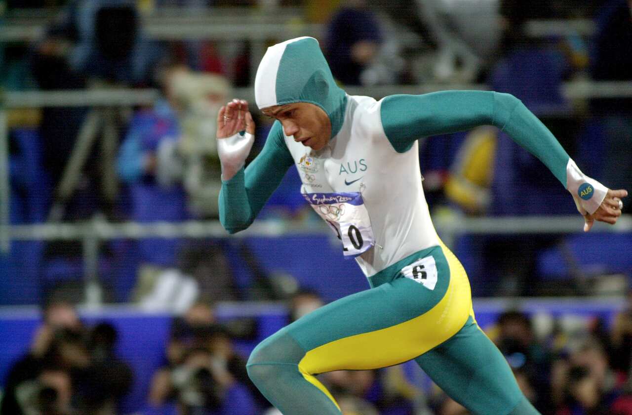 A woman in a green, gold and white track suit runs.