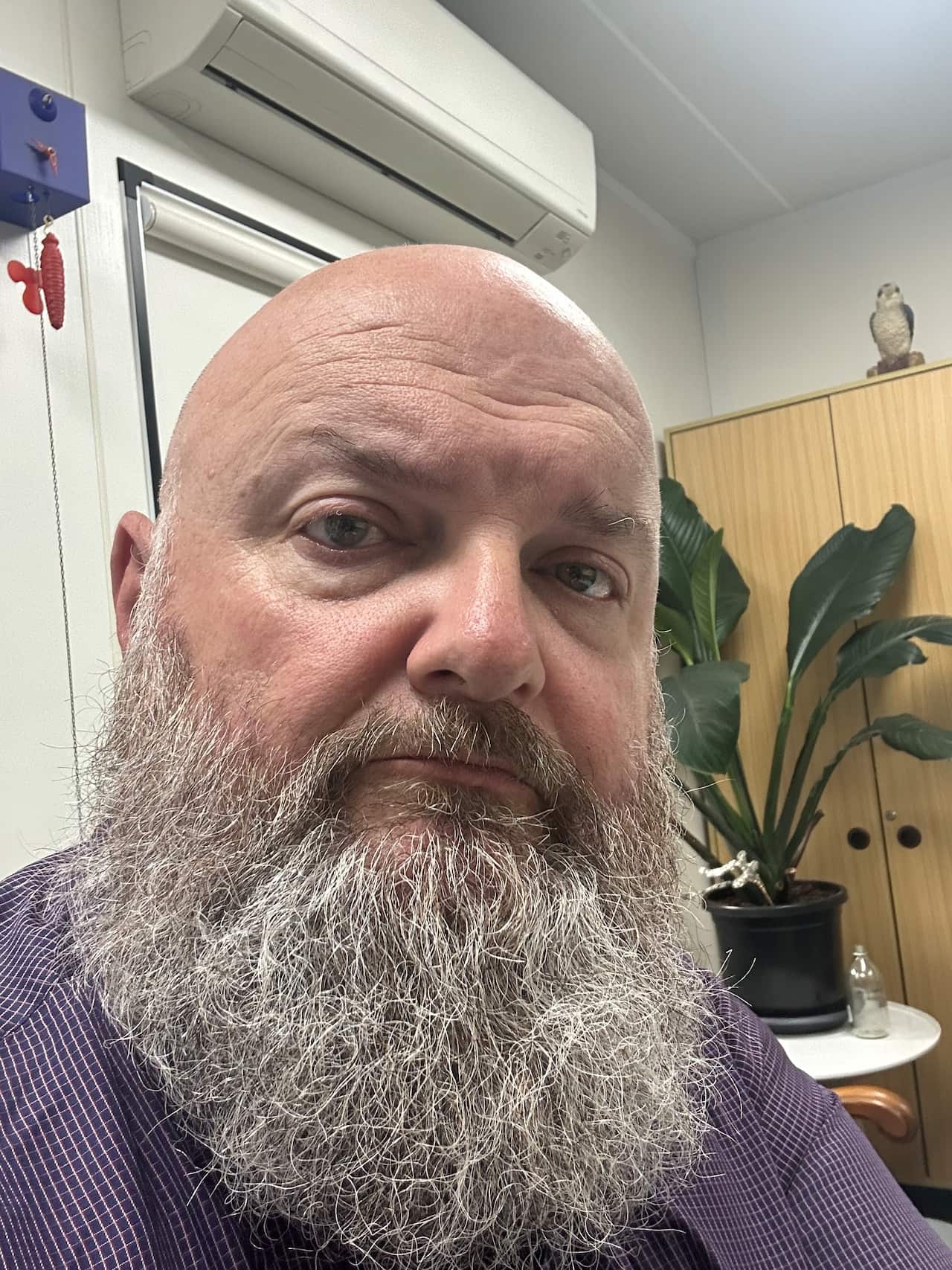 A headshot of a man with a beard looks at the camera with a serious expression on his face.