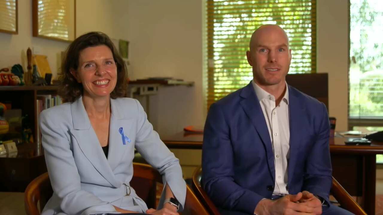 A woman and a man sitting down in an office together, smiling at the camera.