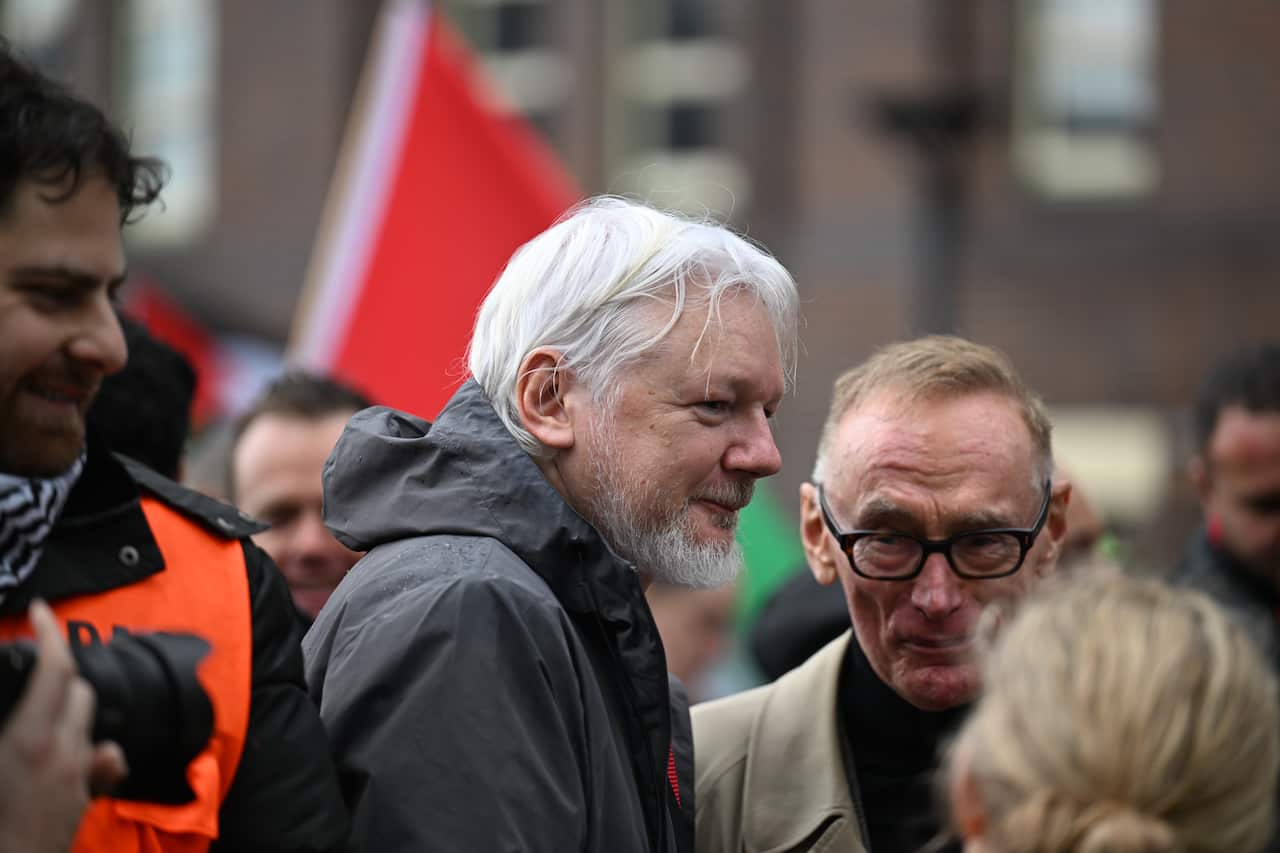 A grey haired man in a black parka stands among a crowd.