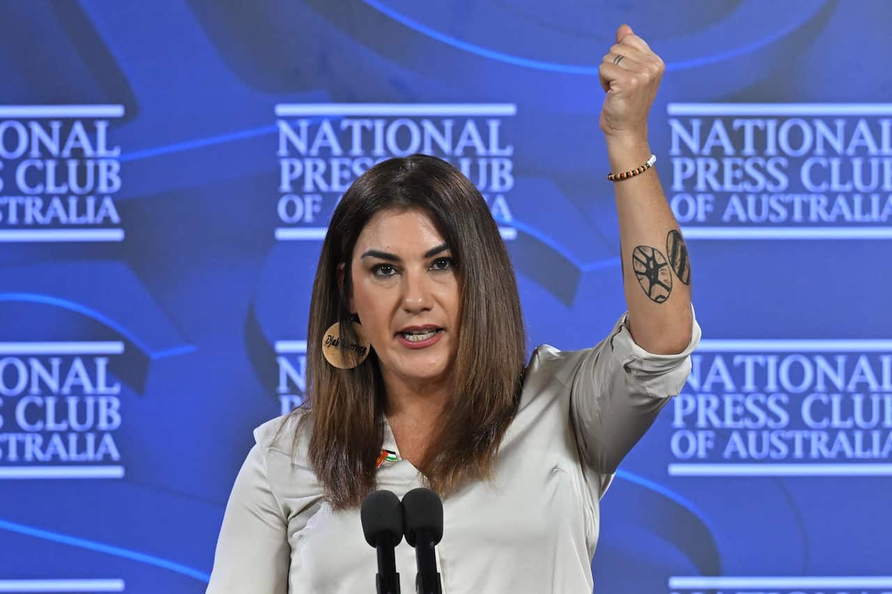 A woman speaks at a lecturn, with one hand raised. 