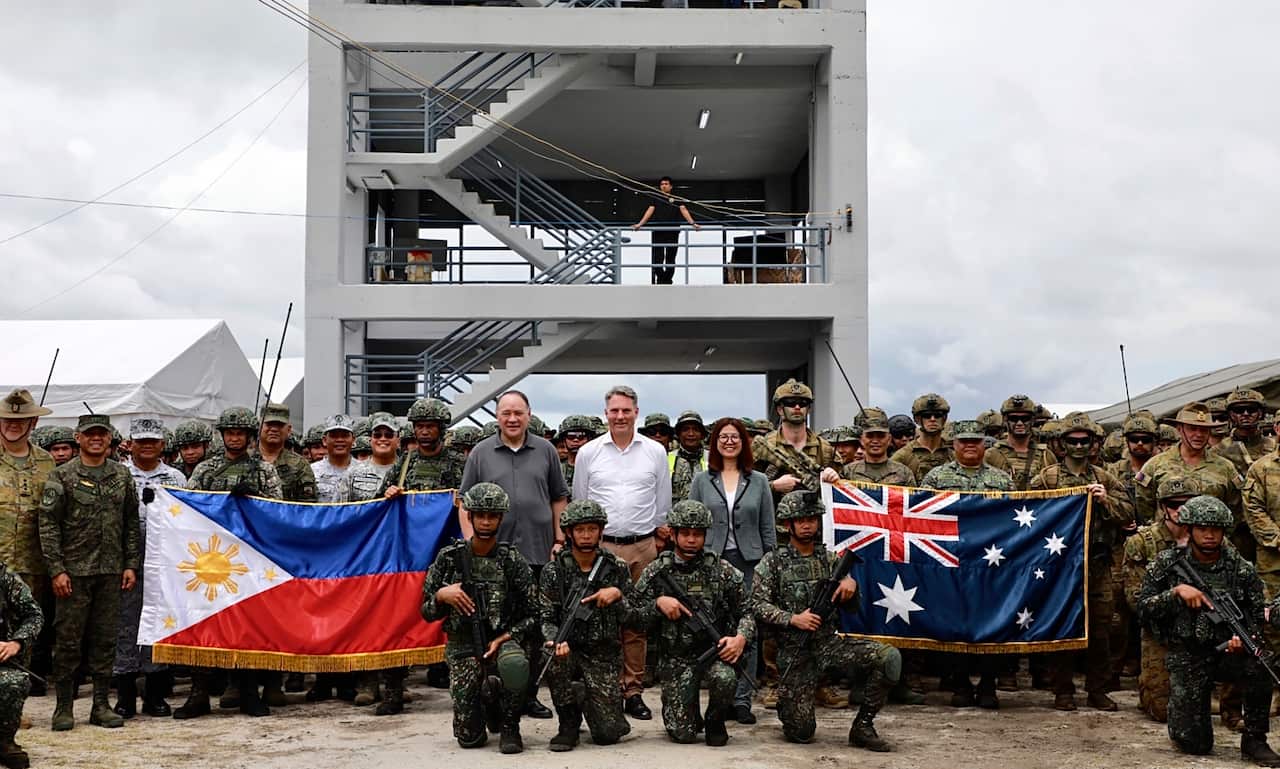 Two men and a woman are flanked by soldiers holding up the flags of Indonesia and Australia. 