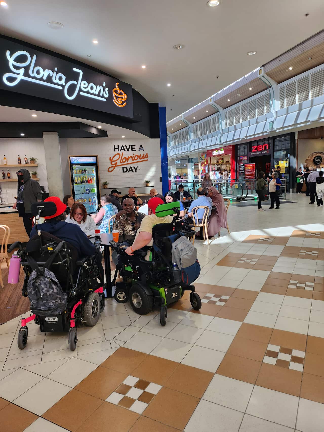 A group of people is sitting at a table outside Gloria Jean's cafe inside a shopping mall.