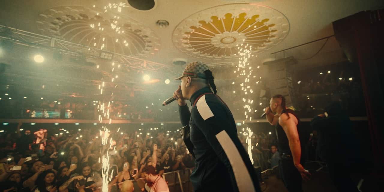 Two men performing on stage inside a small theatre with fireworks going off either side of them