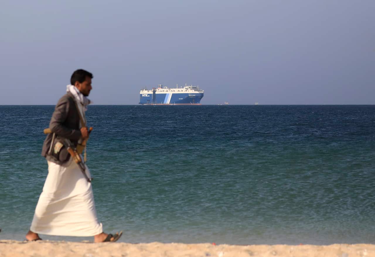 A man walking on a beach with a ship in the background