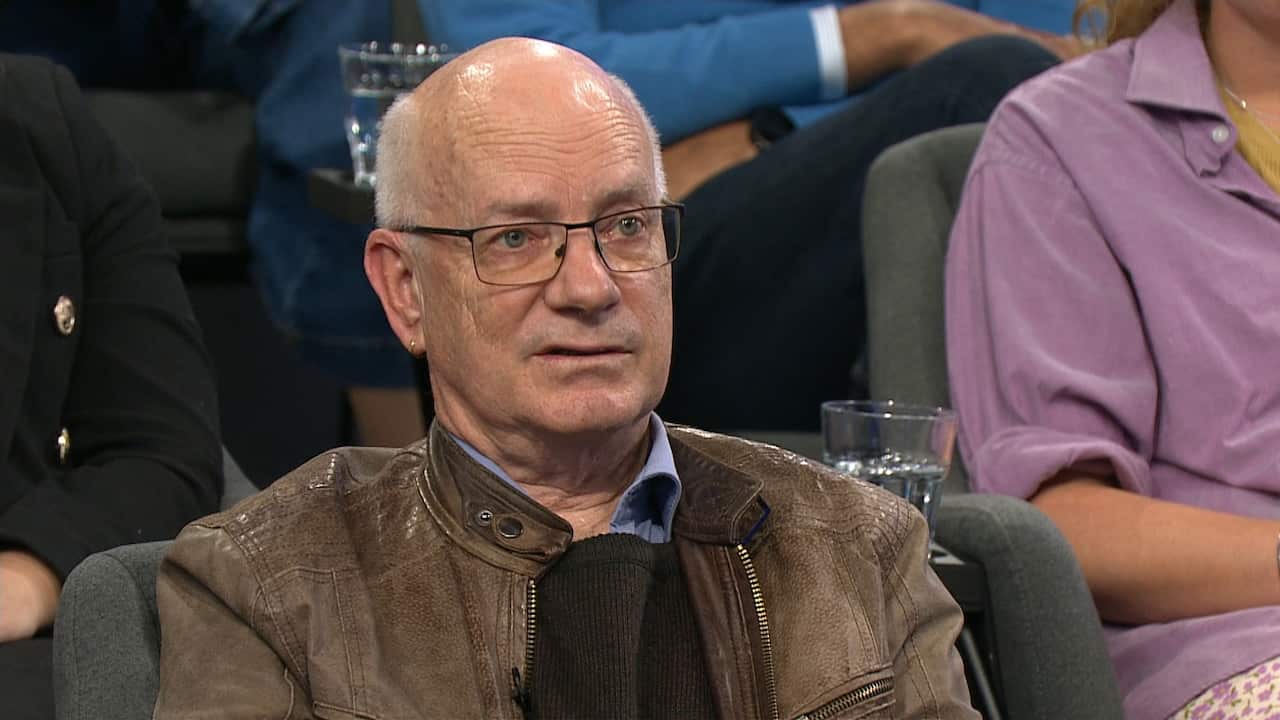 A man with grey hair sits in a TV studio