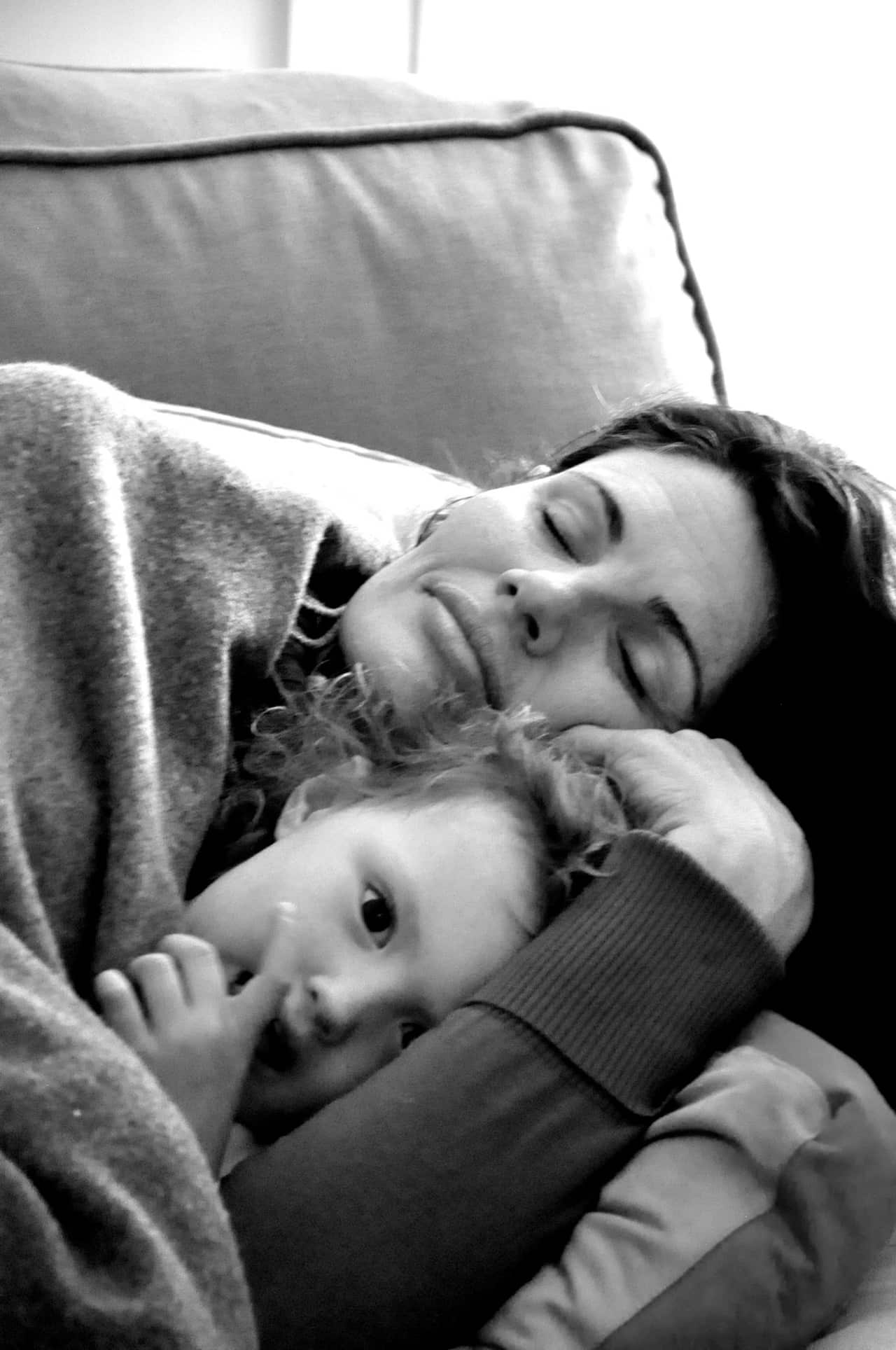 A black and white image of a mother lying down and cuddling her young child.