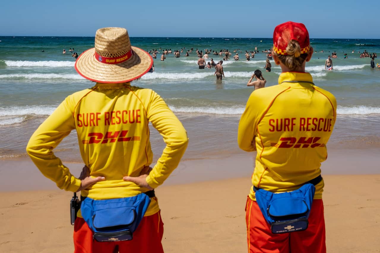 A pair of lifesavers in yellow vests patrol a beach filled with swimmers