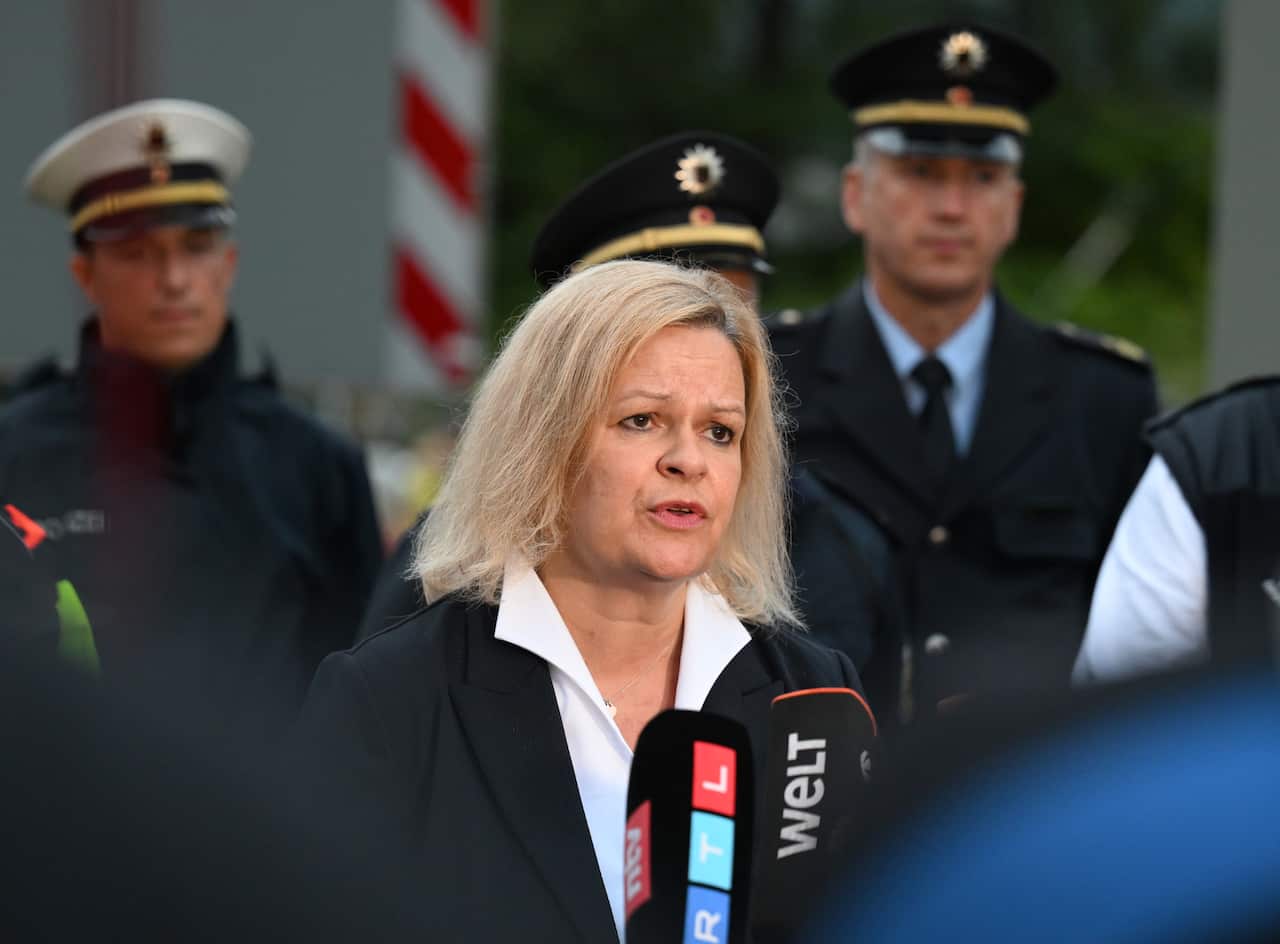A woman speaks to reporters as three officials stand behind her.