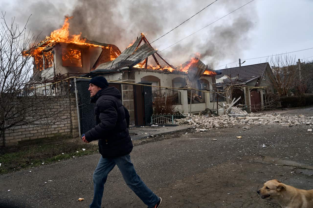 A man runs past a burning house.