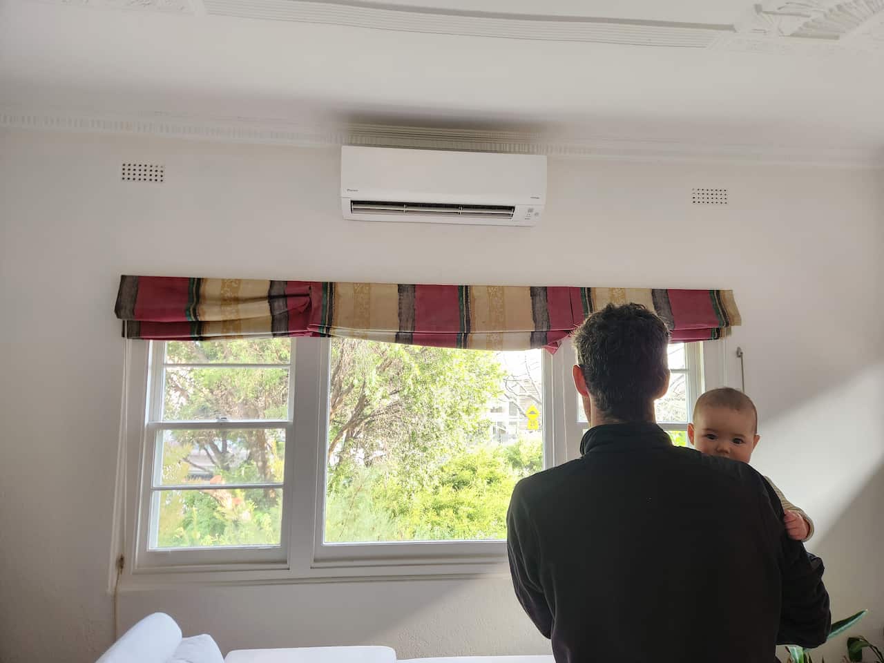 A man looks out of a window while carrying a baby.