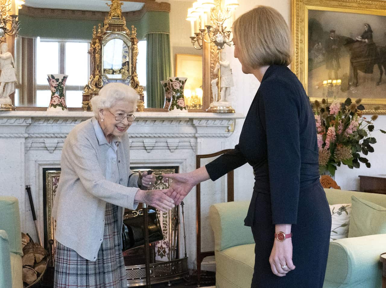The late Queen Elizabeth II and UK Prime Minister Liz Truss extending their arms as they are about to shake hands.