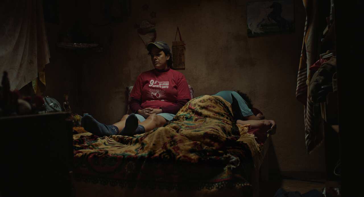 Two people are in a bed, one lying down, the other sitting up.